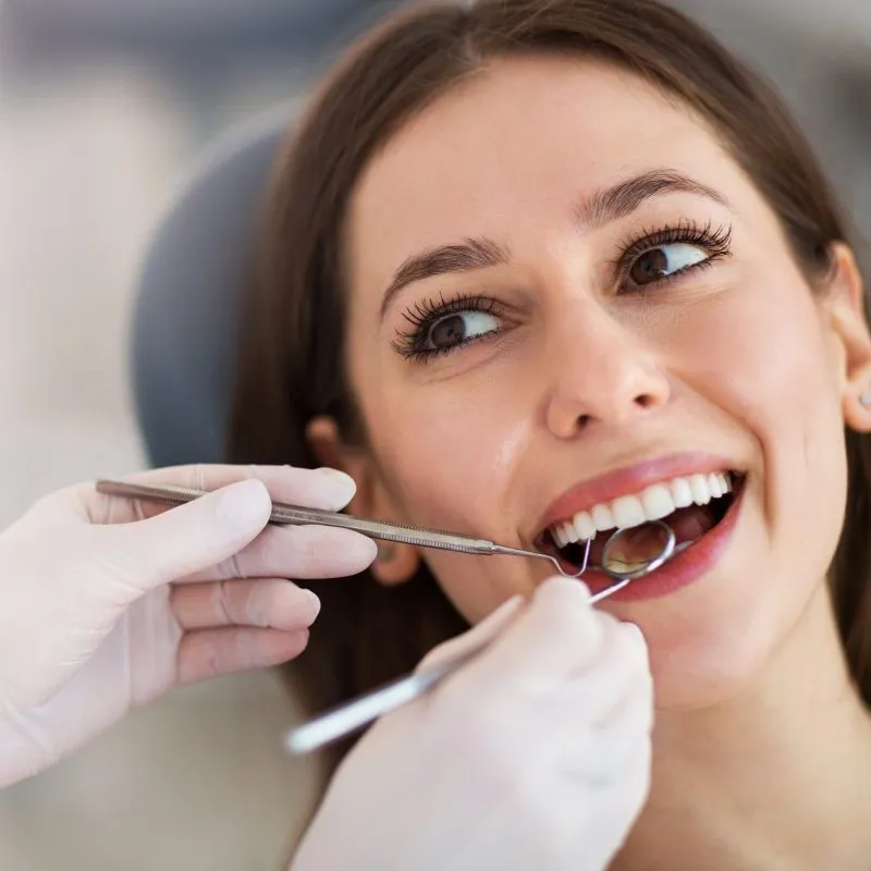 Woman smiling while a dentist examines her mouth using tools