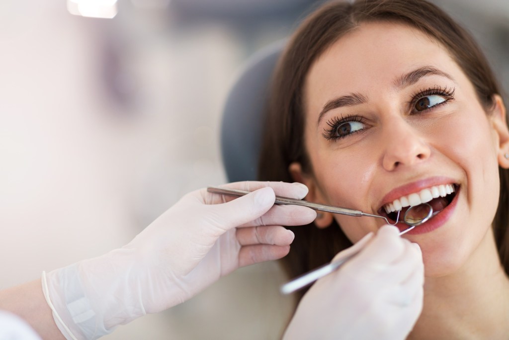 Woman smiling while a dentist examines her mouth using tools